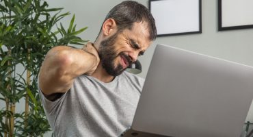 man-experiencing-neck-pain-while-working-from-home-laptop