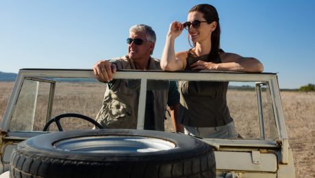 Couple looking away while standing in vehicle on landscape during sunny day